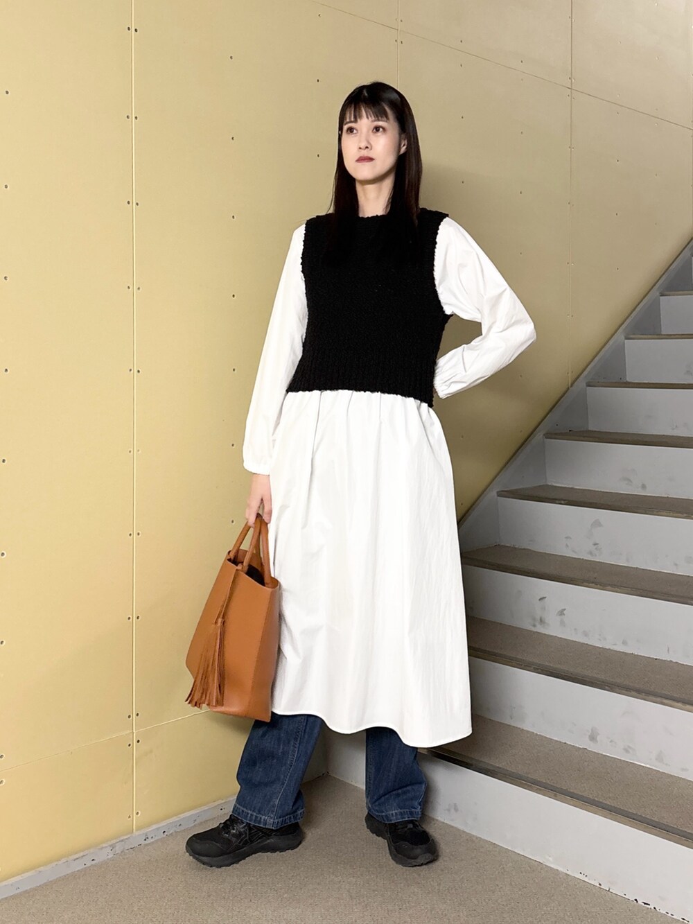 ブラック系のワンピース、ブルー系のデニムパンツ、イエロー系のトートバッグを着用したレディースの冬コーディネートの2枚目の写真