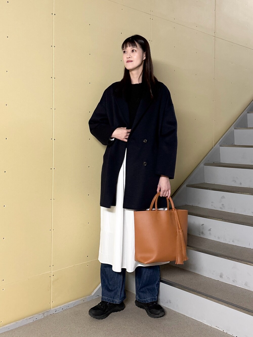 ブラック系のワンピース、ブルー系のデニムパンツ、イエロー系のトートバッグを着用したレディースの冬コーディネートの5枚目の写真