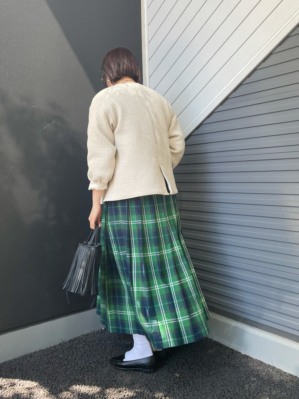 ホワイト系のノーカラージャケット、グリーン系のスカート、ブラック系のハンドバッグを着用したレディースの冬コーディネートの2枚目の写真