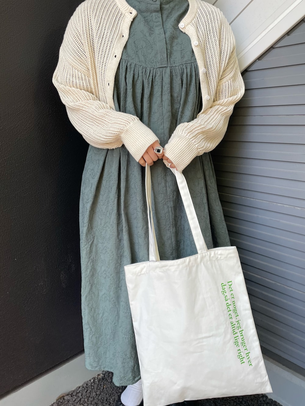 グリーン系のワンピース、ベージュ系のニット/セーター、ホワイト系のトートバッグを着用したレディースの春コーディネートの2枚目の写真