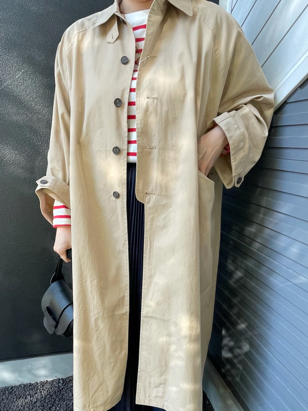 ベージュ系のステンカラーコート、レッド系のTシャツ/カットソー、ブラック系のショルダーバッグを着用したレディースの冬コーディネートの2枚目の写真