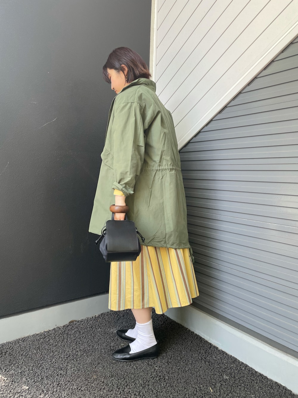 グリーン系のモッズコート、イエロー系のワンピース、ブラック系のスリッポンを着用したレディースの春コーディネートの3枚目の写真