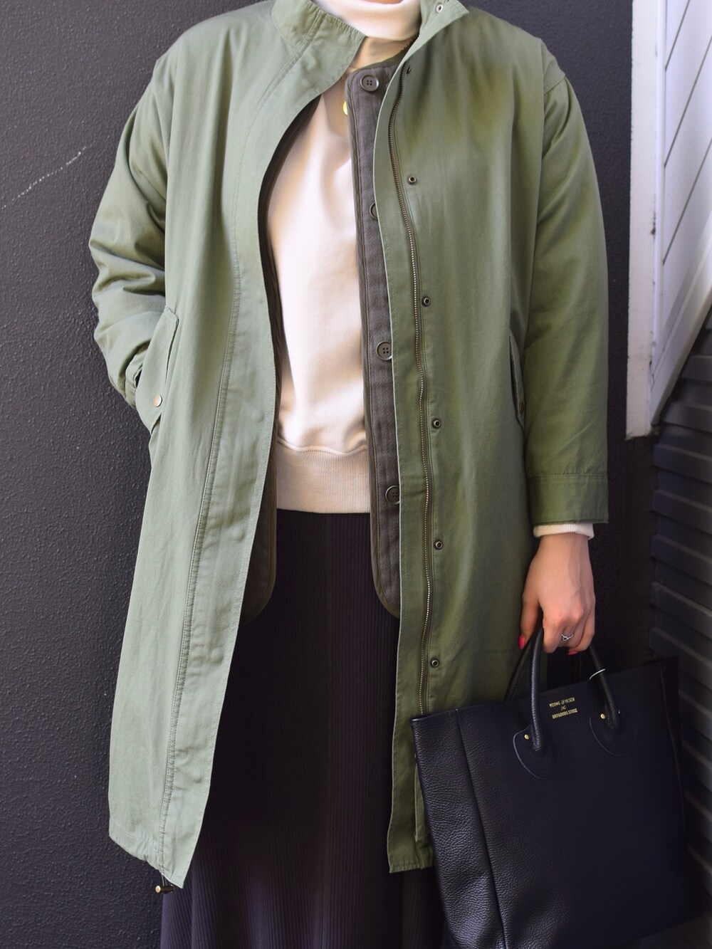 グリーン系のミリタリージャケット、ブラック系のトートバッグ、グレー系のスカートを着用したレディースの冬コーディネートの2枚目の写真