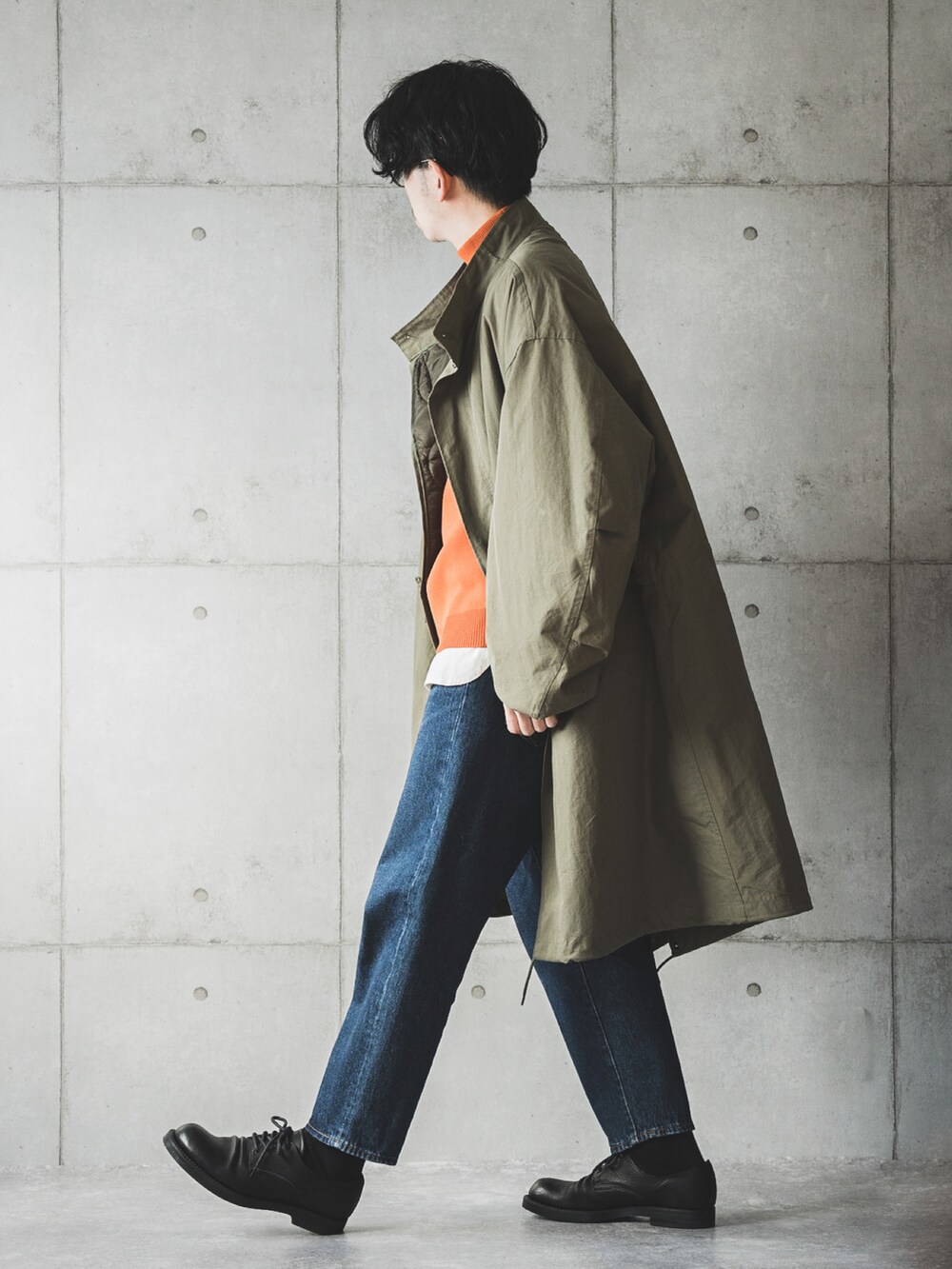 グリーン系のモッズコート、オレンジ系のニット/セーター、ブルー系のデニムパンツを着用したメンズの冬コーディネートの2枚目の写真