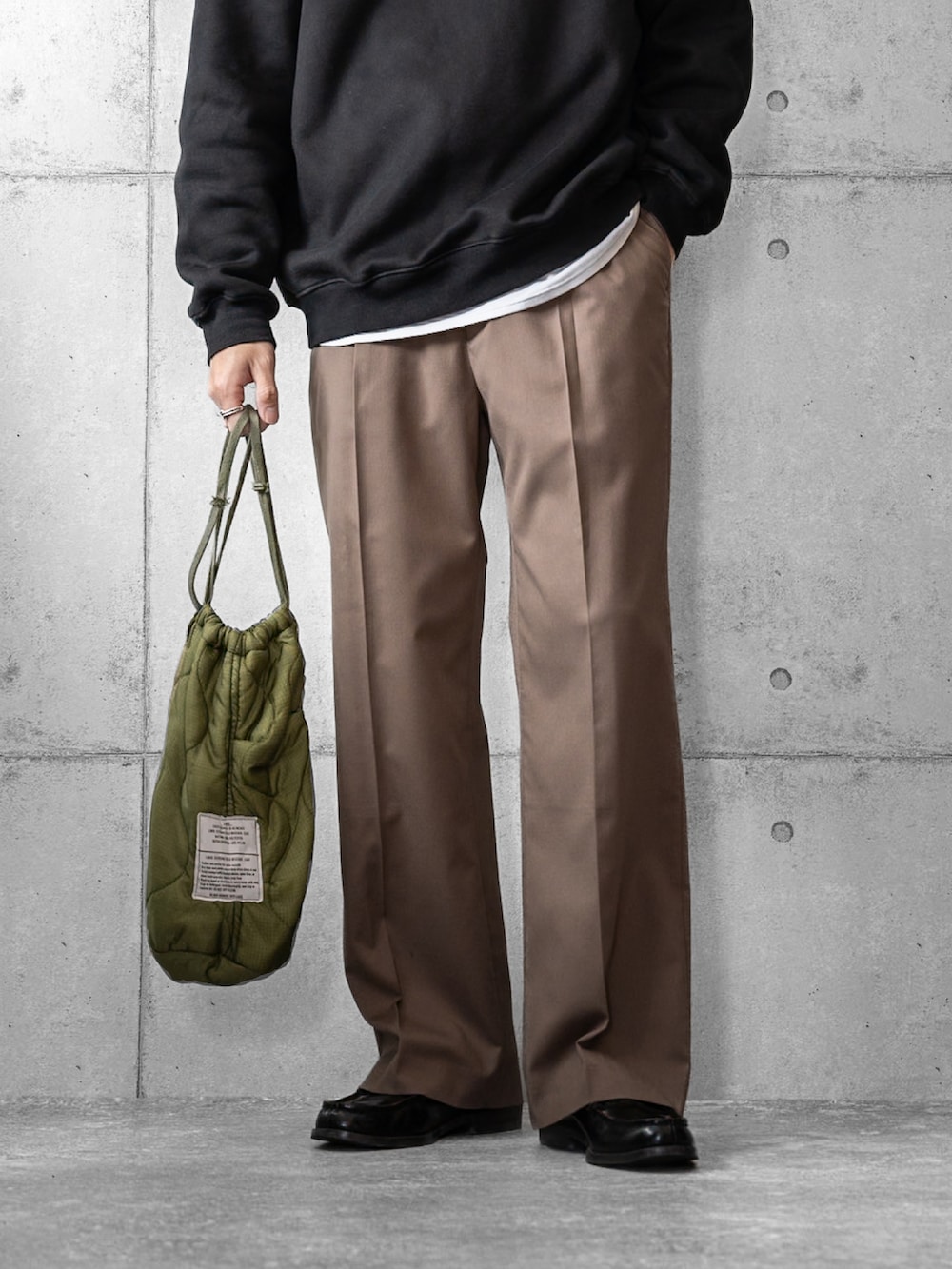 ブラック系のスウェット、ブラウン系のスラックス、グリーン系のショルダーバッグを着用したメンズの春コーディネートの3枚目の写真