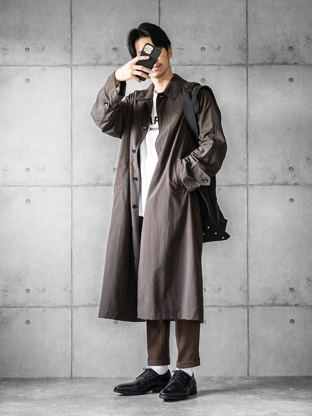 ブラック系のドレスシューズ、ブラック系のトートバッグ、ブラウン系のステンカラーコートを着用したメンズの秋コーディネートの2枚目の写真