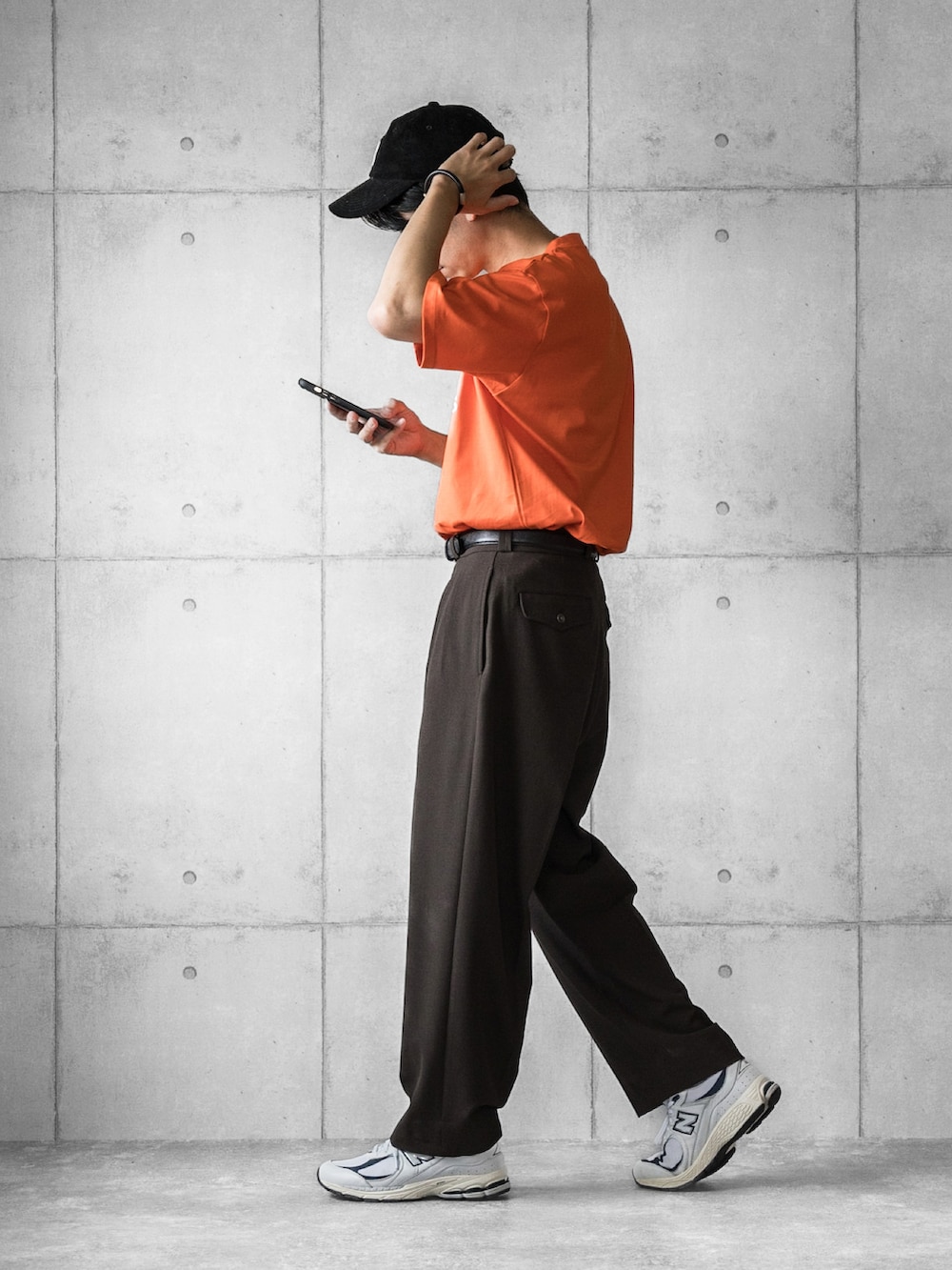 オレンジ系のTシャツ/カットソー、ブラウン系のスラックス、ホワイト系のスニーカーを着用したメンズの夏コーディネートの3枚目の写真