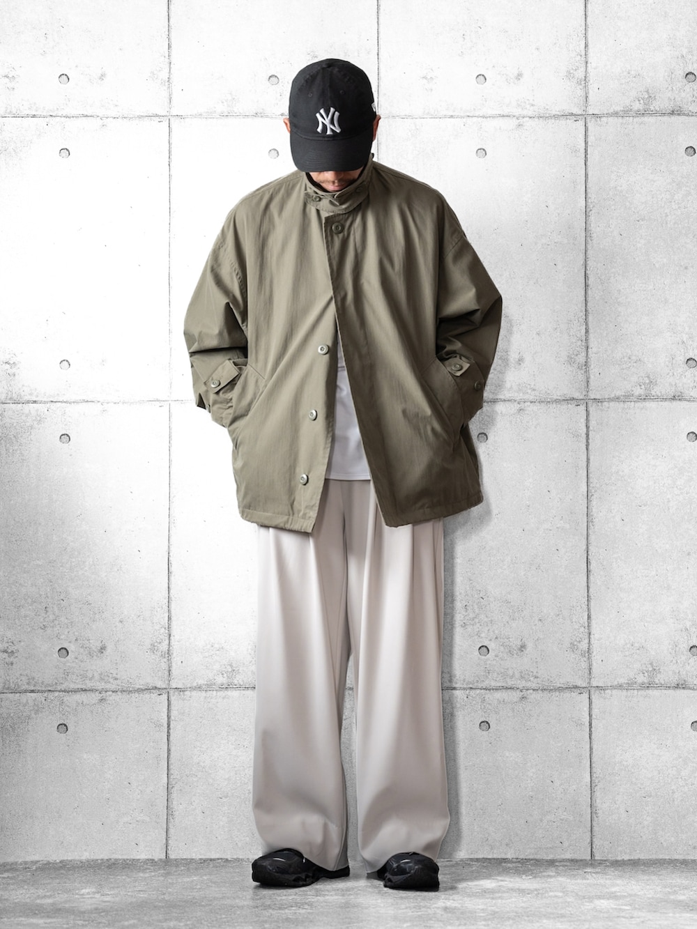 ホワイト系のスラックス、ブラック系のスニーカー、グリーン系のブルゾンを着用したメンズの春コーディネートの2枚目の写真