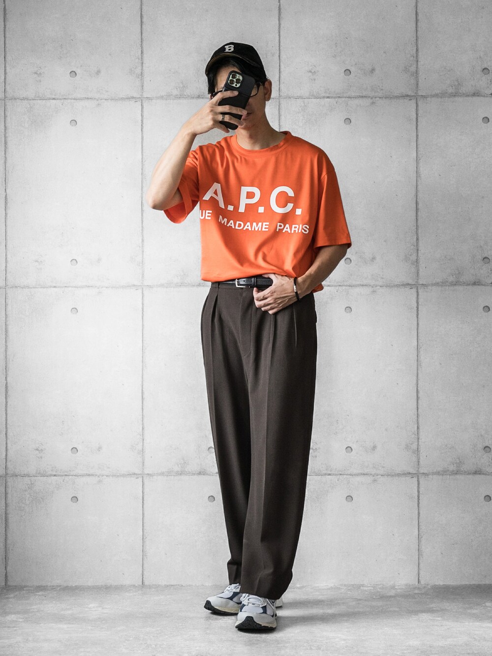 オレンジ系のTシャツ/カットソー、ブラウン系のスラックス、ホワイト系のスニーカーを着用したメンズの夏コーディネートの2枚目の写真