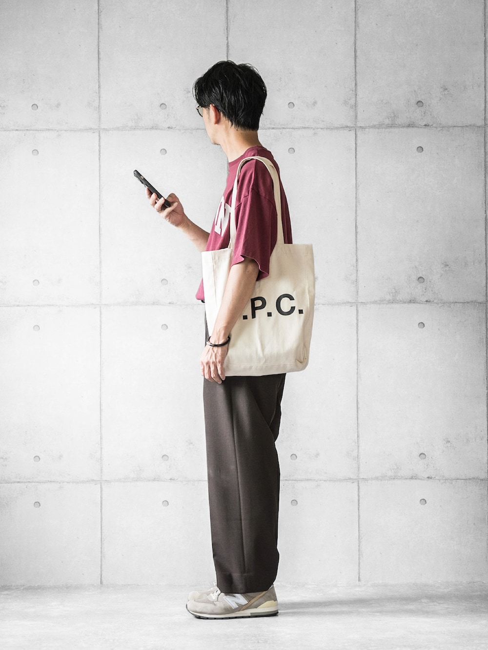 レッド系のTシャツ/カットソー、ブラウン系のスラックス、ホワイト系のトートバッグを着用したメンズの夏コーディネートの2枚目の写真