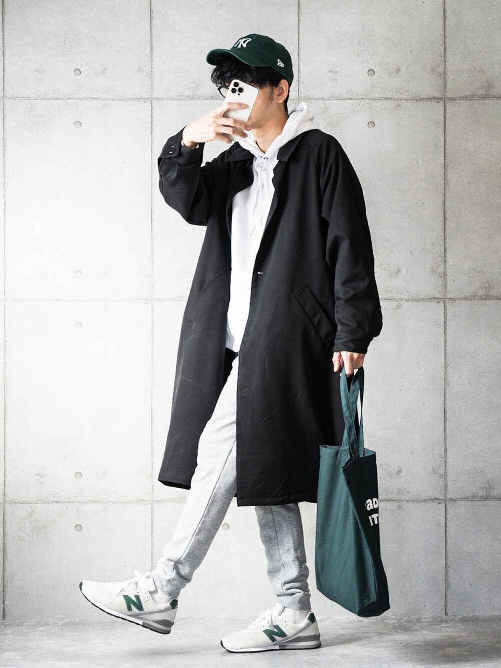 ブラック系のステンカラーコート、ホワイト系のパーカー、グリーン系のトートバッグを着用したメンズの秋コーディネートの2枚目の写真