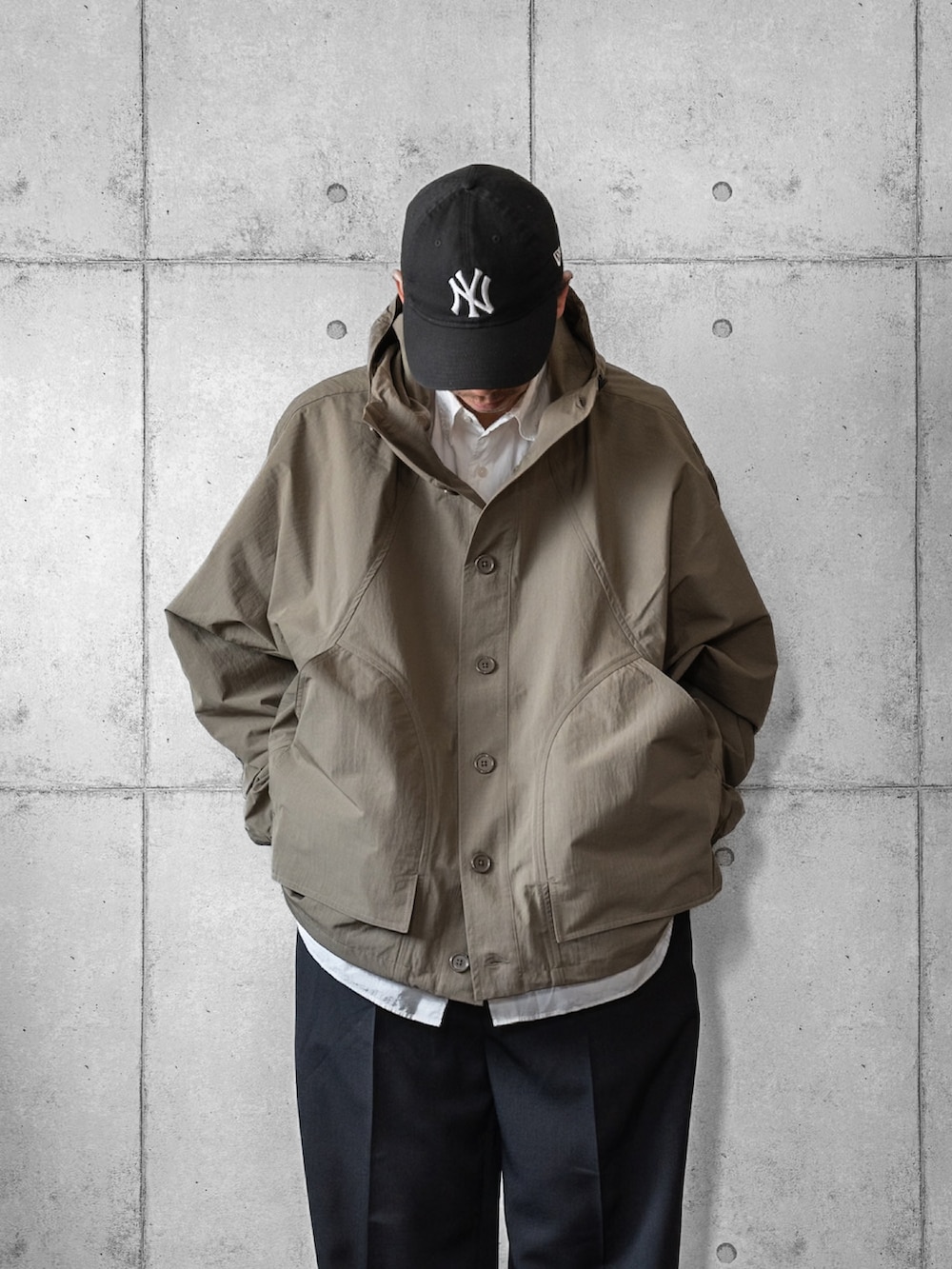 グリーン系のポンチョ、ブラック系のスラックス、ホワイト系のシャツ/ブラウスを着用したメンズの春コーディネートの2枚目の写真