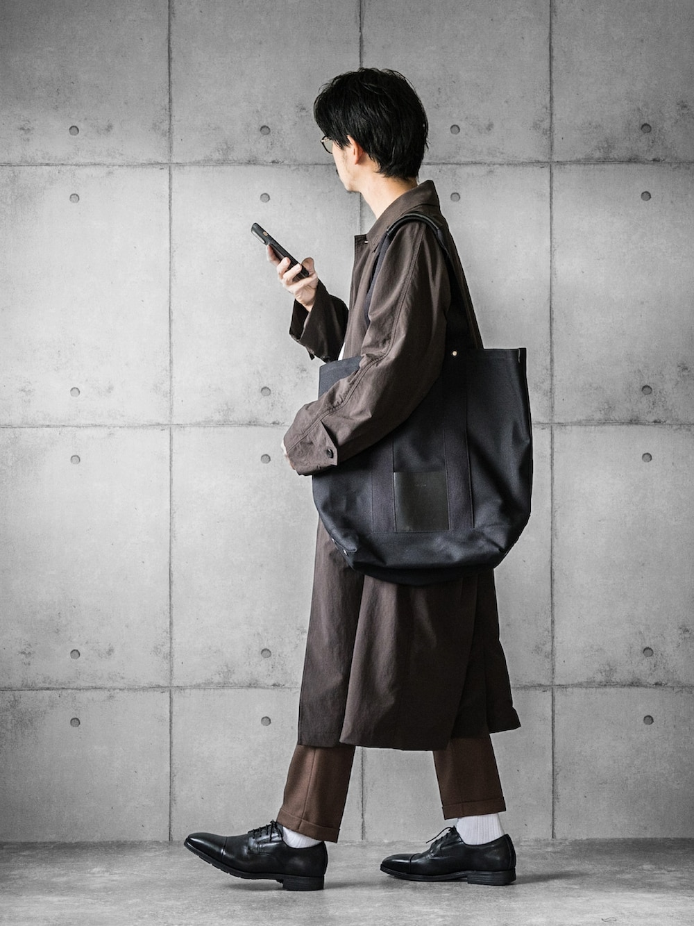 ブラック系のドレスシューズ、ブラック系のトートバッグ、ブラウン系のステンカラーコートを着用したメンズの秋コーディネートの4枚目の写真