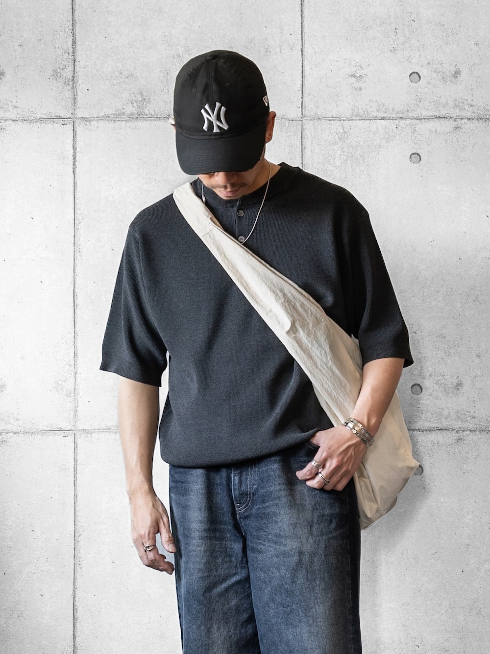 グレー系のニット/セーター、ブルー系のデニムパンツ、ホワイト系のショルダーバッグを着用したメンズの春コーディネートの2枚目の写真