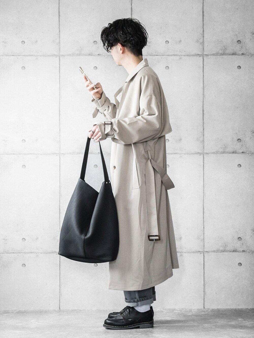 グレー系のデニムパンツ、ブルー系のニット/セーター、ベージュ系のトレンチコートを着用したメンズの春コーディネートの2枚目の写真