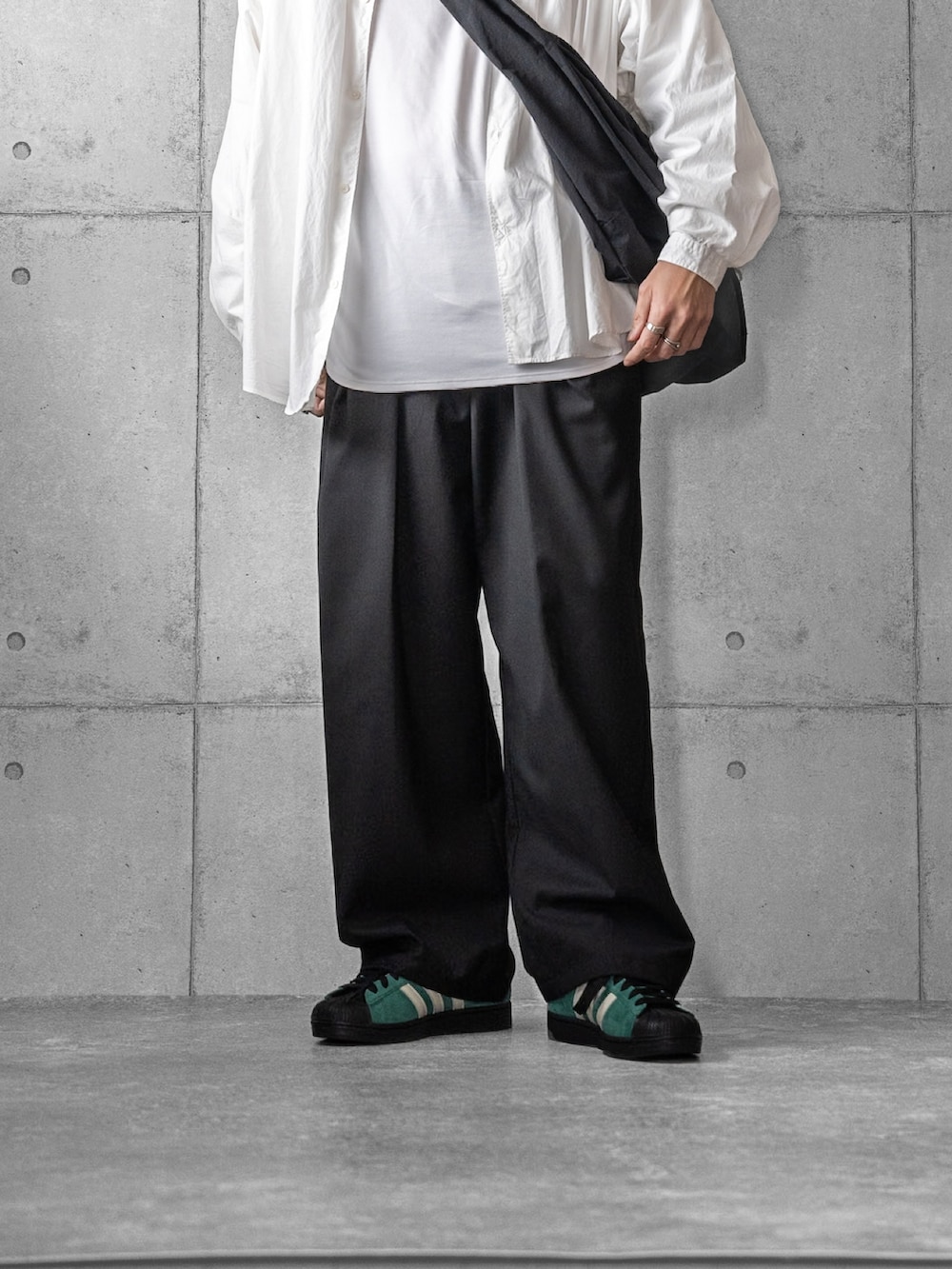 グリーン系のスニーカー、ブラック系のスラックス、ブラック系のショルダーバッグを着用したメンズの春コーディネートの3枚目の写真