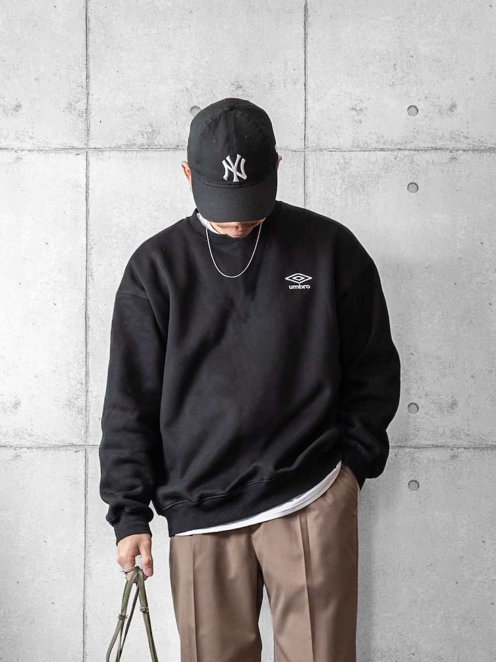 ブラック系のスウェット、ブラウン系のスラックス、グリーン系のショルダーバッグを着用したメンズの春コーディネートの2枚目の写真