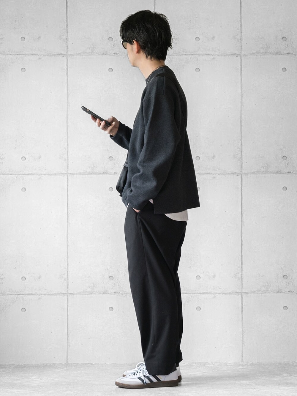グレー系のニット/セーター、ブラック系のスラックス、ブラック系のショルダーバッグを着用したメンズの春コーディネートの2枚目の写真