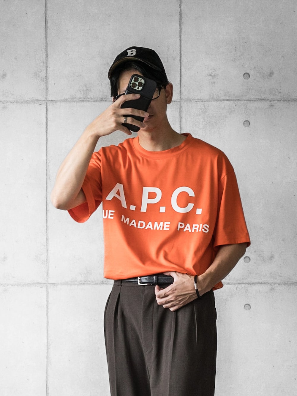 オレンジ系のTシャツ/カットソー、ブラウン系のスラックス、ホワイト系のスニーカーを着用したメンズの夏コーディネートの4枚目の写真