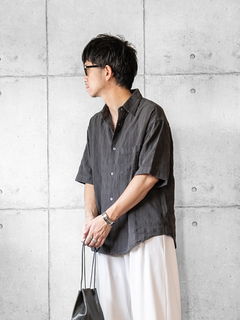 グレー系のシャツ/ブラウス、ホワイト系のスラックス、ブラック系のショルダーバッグを着用したメンズの夏コーディネートの2枚目の写真