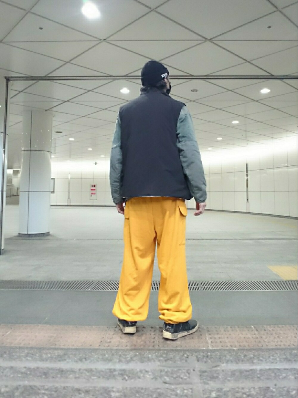 グレー系のミリタリージャケット、ブラック系のダウンベスト、イエロー系のカーゴパンツを着用したメンズの春コーディネートの2枚目の写真