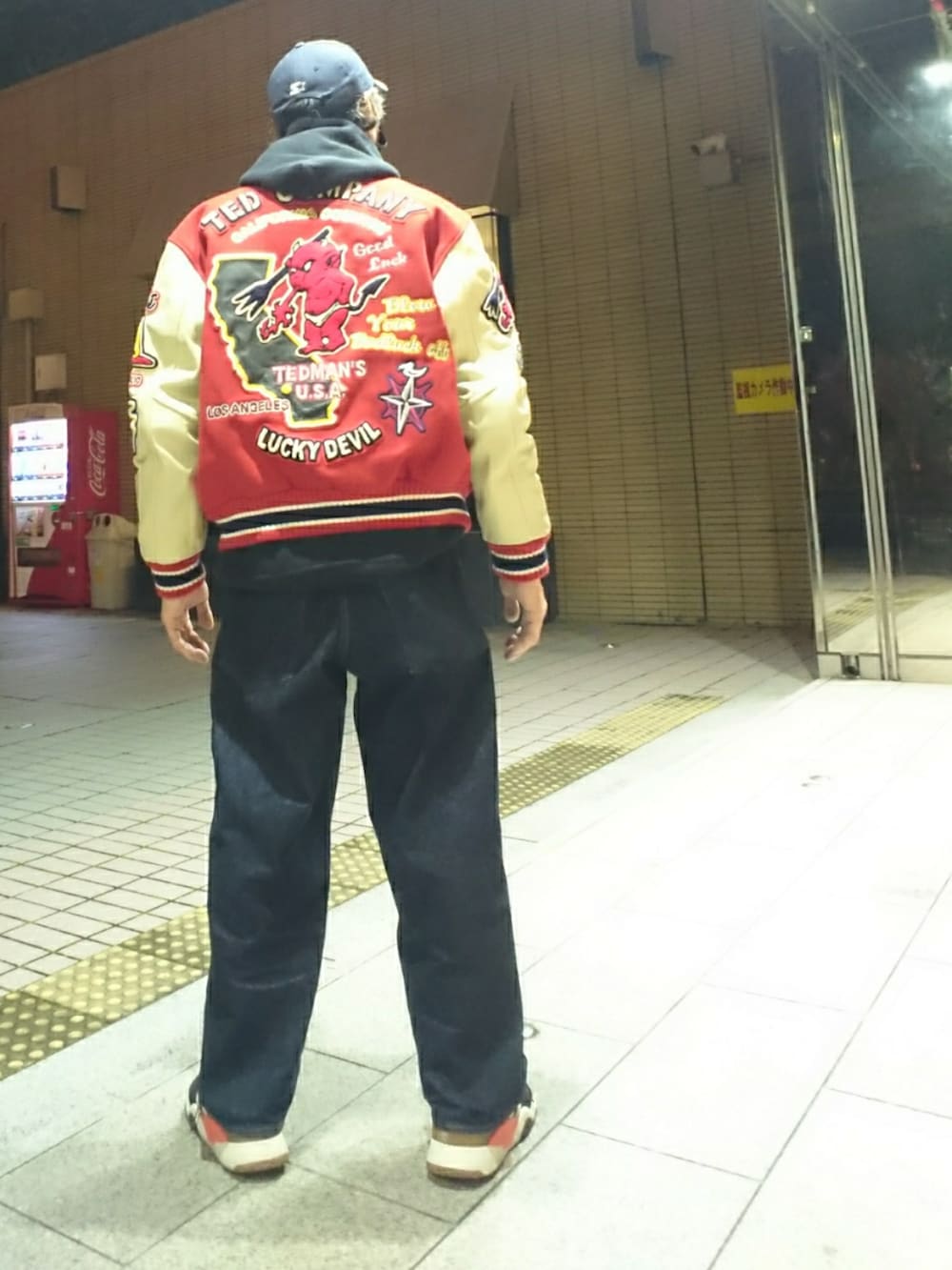 レッド系のスタジャン、ブラック系のパーカー、ブルー系のデニムパンツを着用したメンズの冬コーディネートの2枚目の写真