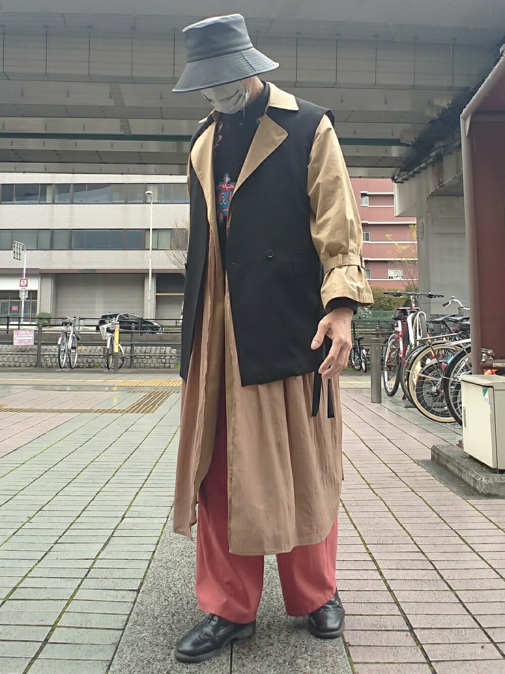 ブラック系のベスト、ブラック系のニット/セーター、ブラウン系のトレンチコートを着用したメンズの春コーディネートの2枚目の写真