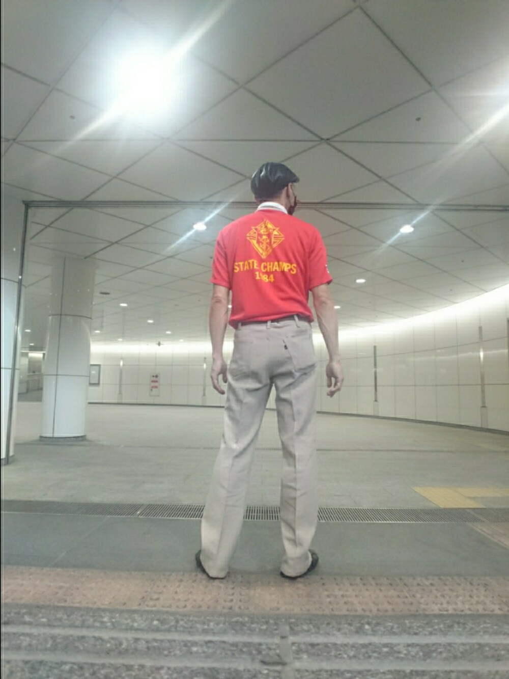 レッド系のトップス、ベージュ系のスラックス、ブラック系のサンダルを着用したメンズの夏コーディネートの2枚目の写真