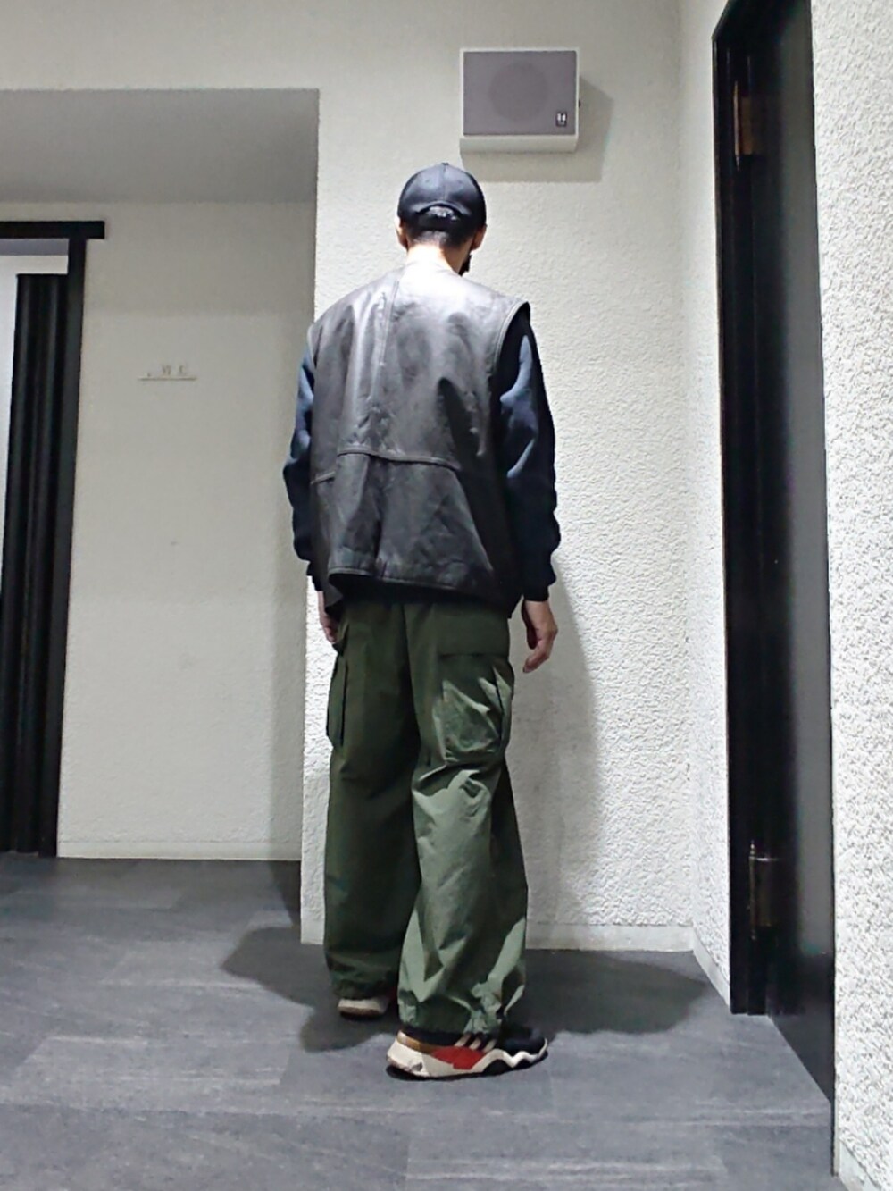 ブラック系のベスト、グリーン系のカーゴパンツ、ブラック系のスニーカーを着用したメンズの春コーディネートの2枚目の写真