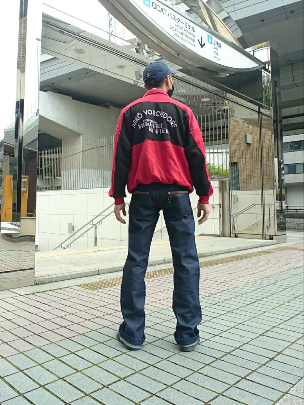 レッド系のジャージ、ブルー系のデニムパンツ、ブラック系のドレスシューズを着用したメンズの春コーディネートの2枚目の写真
