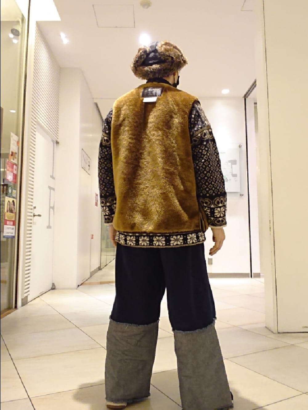 ブラウン系のベスト、ブルー系のデニムパンツ、ブラック系のスニーカーを着用したメンズの冬コーディネートの2枚目の写真