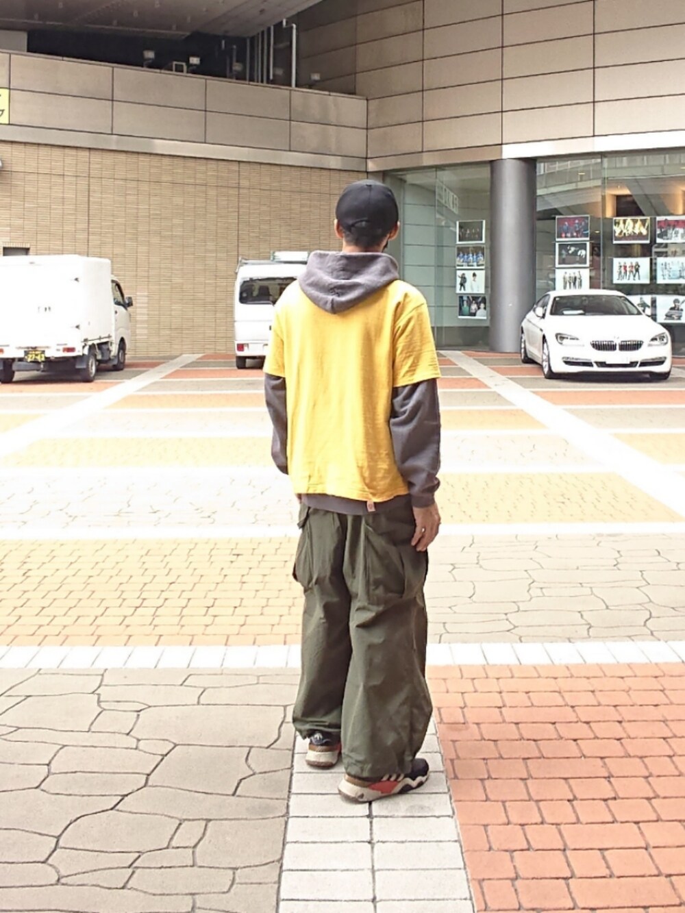 イエロー系のTシャツ/カットソー、グリーン系のカーゴパンツ、ブラック系のスニーカーを着用したメンズの春コーディネートの2枚目の写真