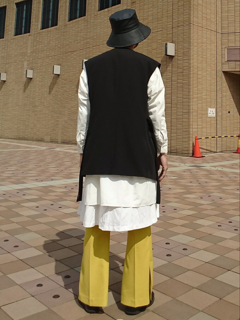 ブラック系のベスト、イエロー系のその他パンツ、ブラック系のサンダルを着用したメンズの春コーディネートの2枚目の写真