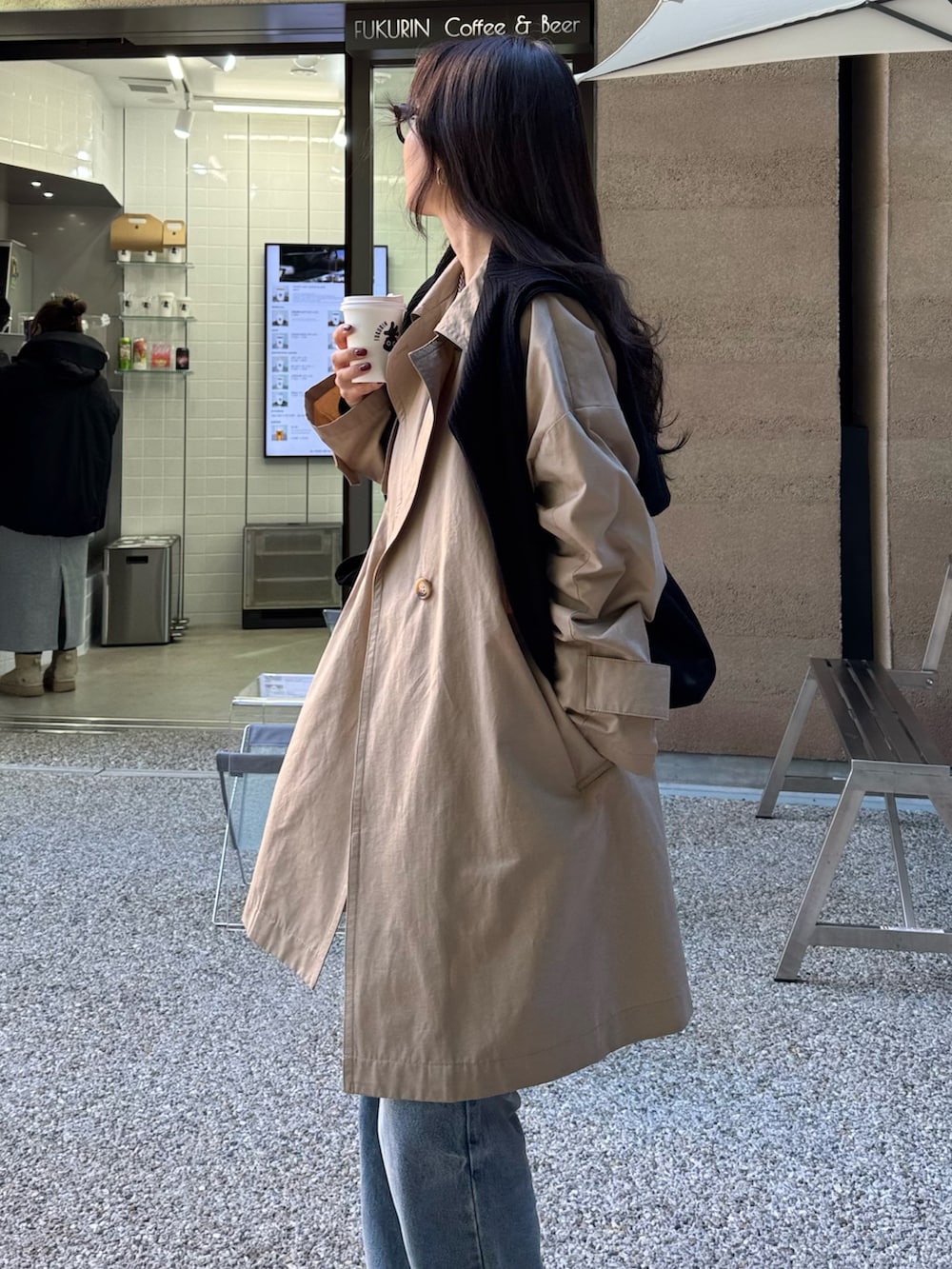 ベージュ系のトレンチコート、ブルー系のデニムパンツ、ブラック系のトートバッグを着用したレディースの冬コーディネートの4枚目の写真