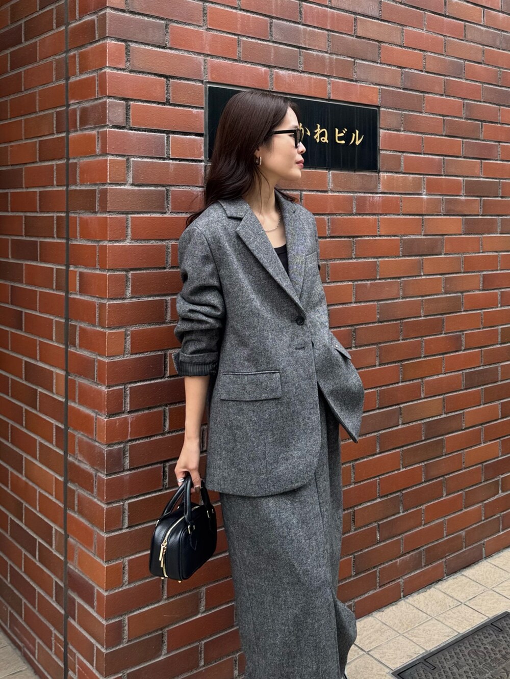 グレー系のテーラードジャケット、グレー系のスカート、ブラック系のショルダーバッグを着用したレディースの秋コーディネートの2枚目の写真