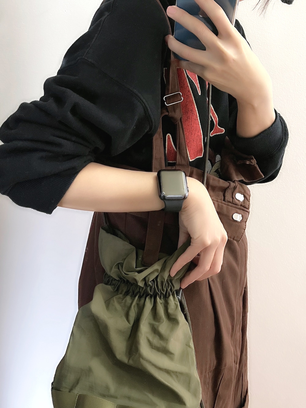 ブラウン系のジャンパースカート、グリーン系のショルダーバッグ、ブラック系のスウェットを着用したレディースの春コーディネートの4枚目の写真