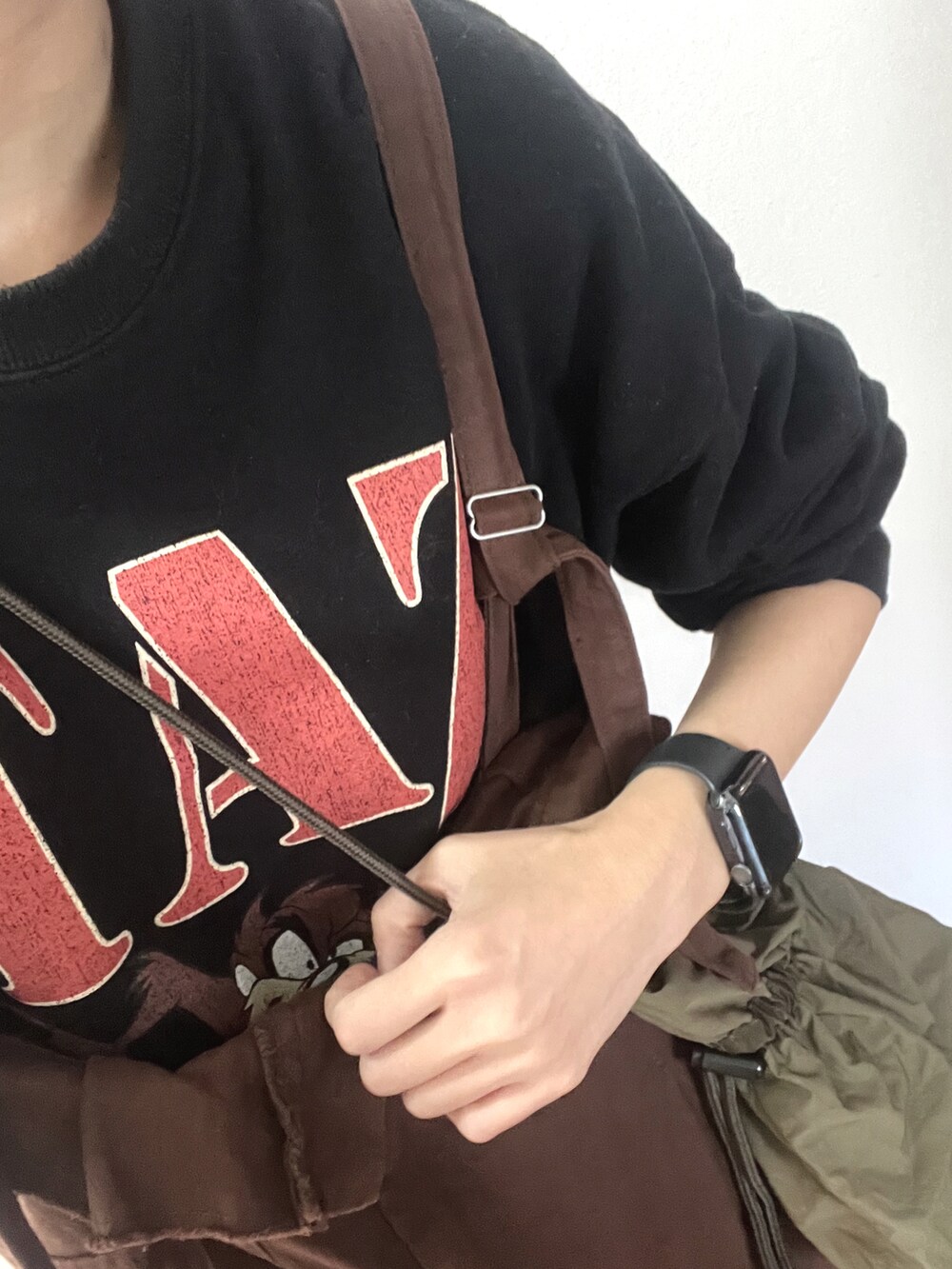 ブラウン系のジャンパースカート、グリーン系のショルダーバッグ、ブラック系のスウェットを着用したレディースの春コーディネートの3枚目の写真