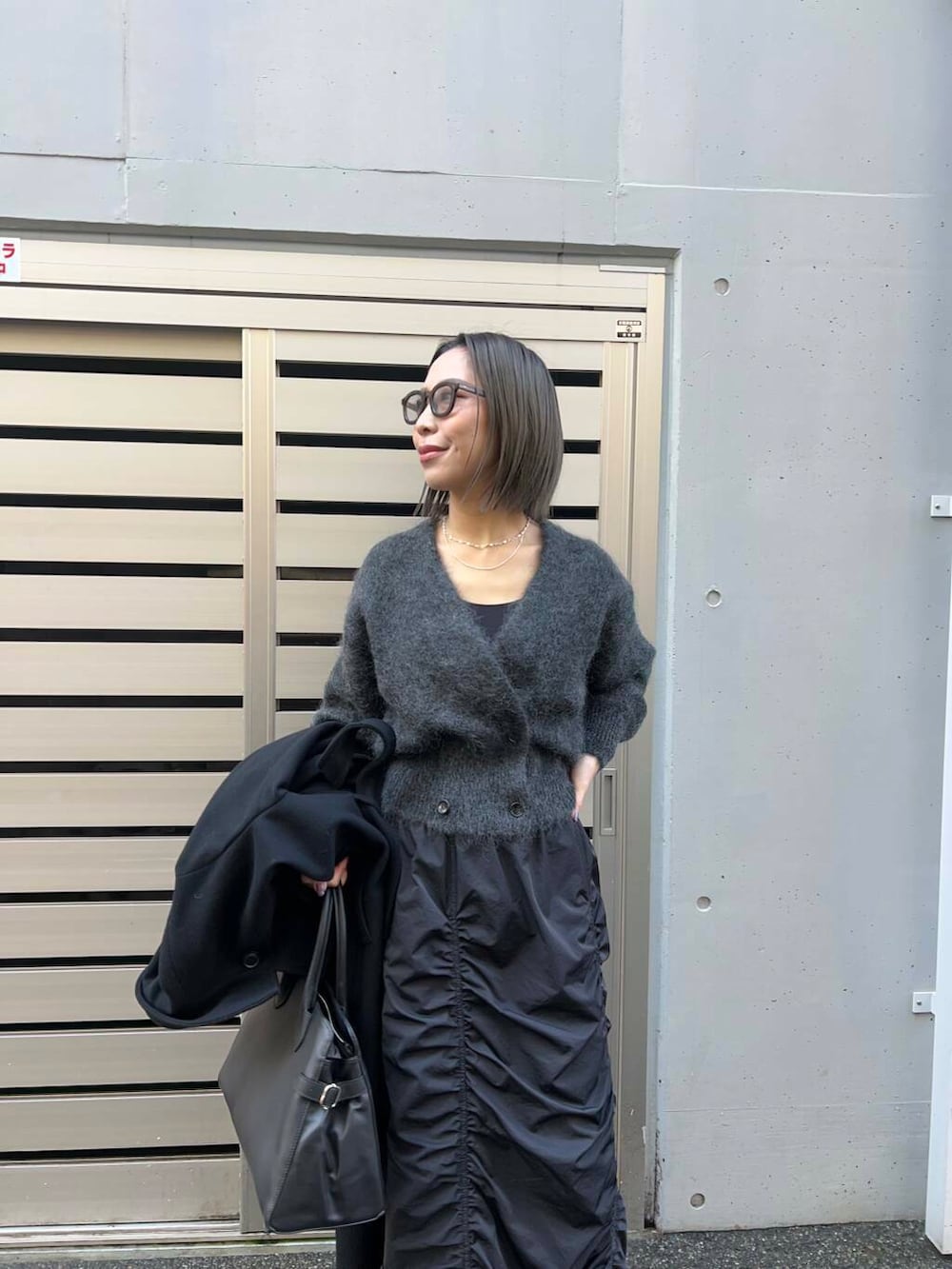 ブラック系のチェスターコート、ブラック系のスカート、グレー系のカーディガン/ボレロを着用したレディースの冬コーディネートの2枚目の写真