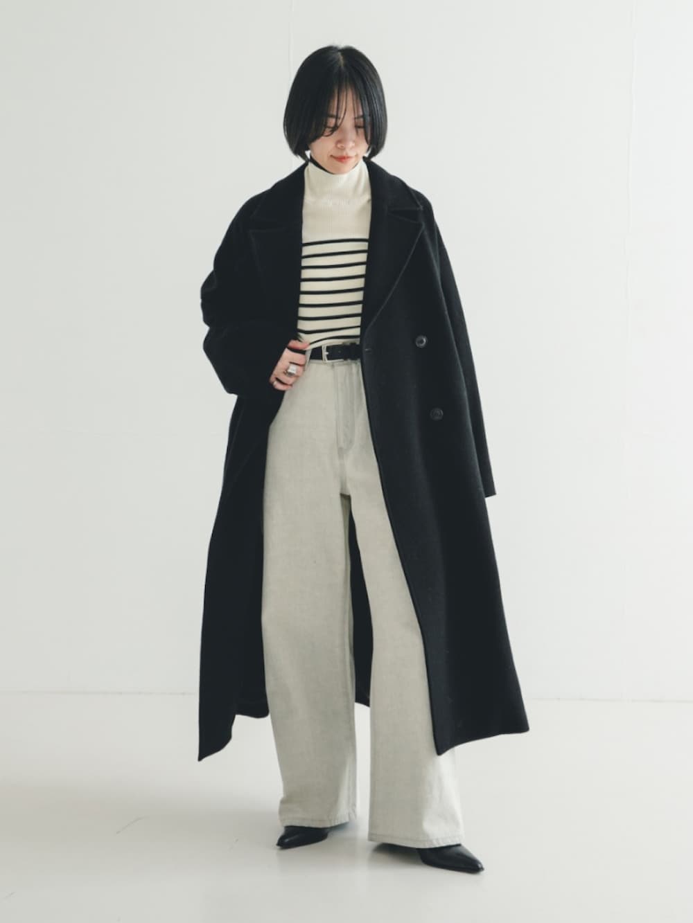 ブラック系のチェスターコート、ホワイト系のニット/セーター、グレー系のデニムパンツを着用したレディースの冬コーディネートの2枚目の写真