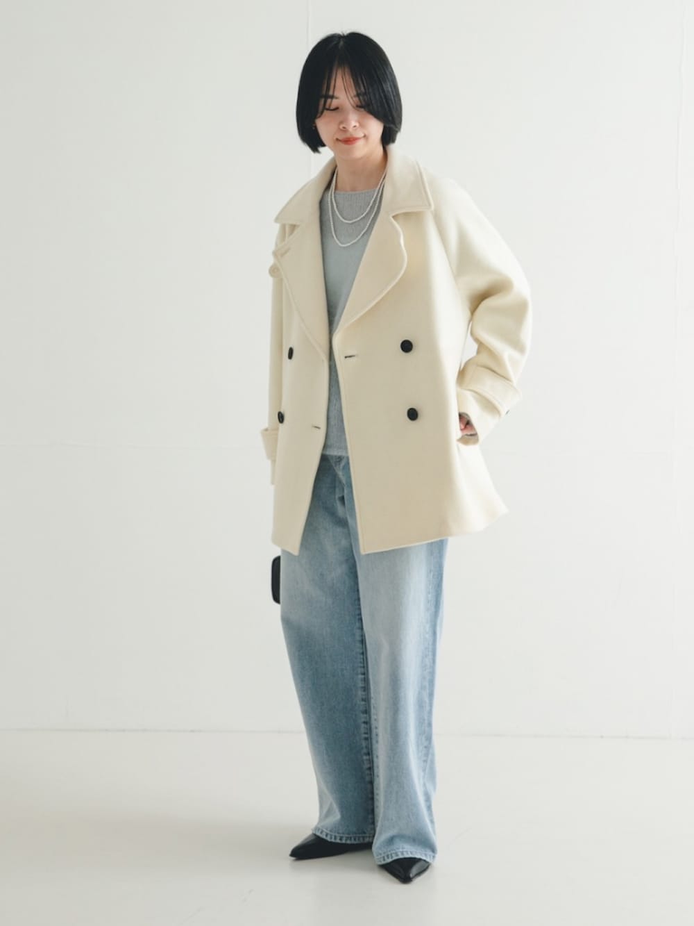 ブルー系のデニムパンツ、ホワイト系のピーコート、ブルー系のニット/セーターを着用したレディースの冬コーディネートの2枚目の写真