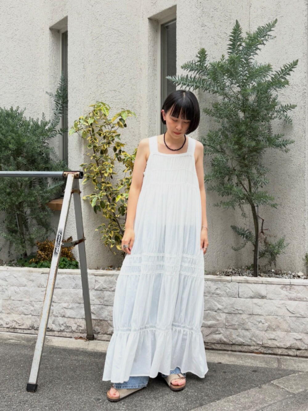 ホワイト系のワンピース、ブルー系のデニムパンツ、ベージュ系のサンダルを着用したレディースの夏コーディネートの2枚目の写真