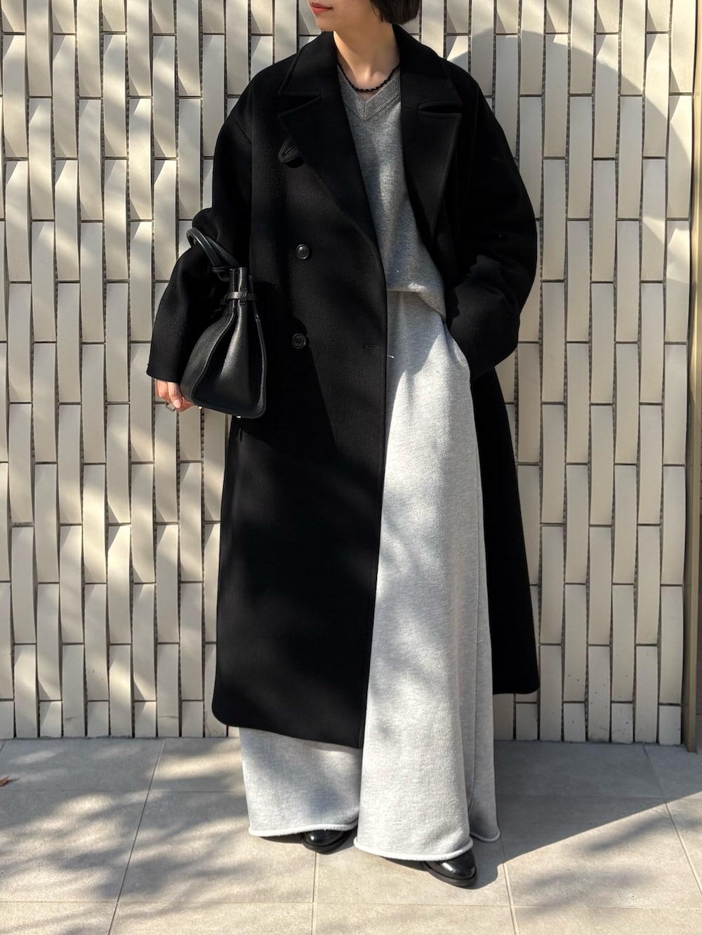 ブラック系のトートバッグ、ブラック系のチェスターコート、グリーン系のニット/セーターを着用したレディースの冬コーディネートの2枚目の写真