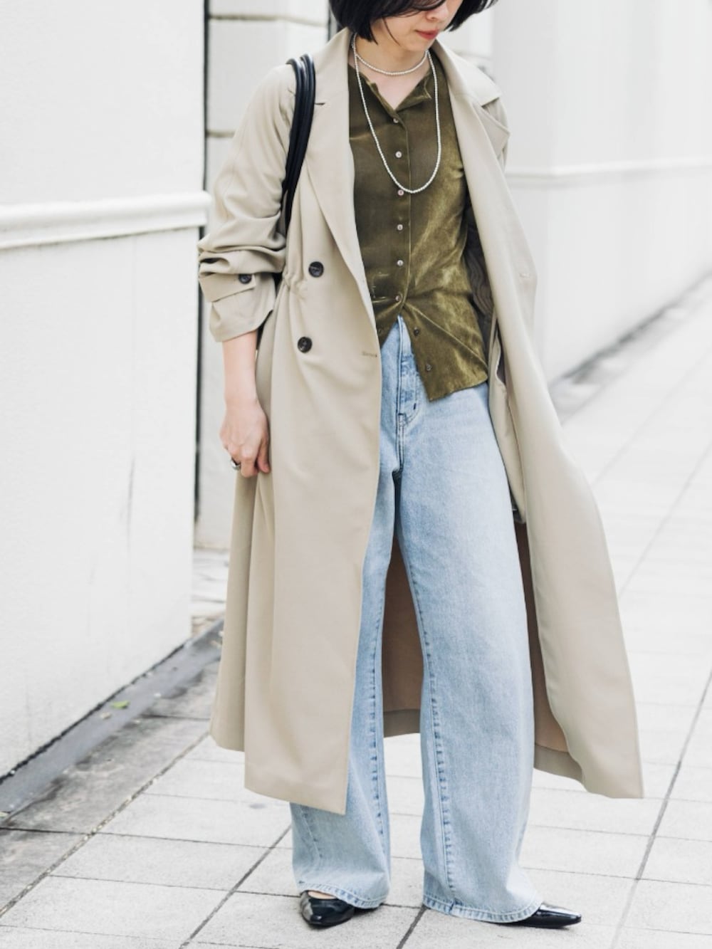 ベージュ系のトレンチコート、グリーン系のカーディガン/ボレロ、ブルー系のデニムパンツを着用したレディースの冬コーディネートの2枚目の写真