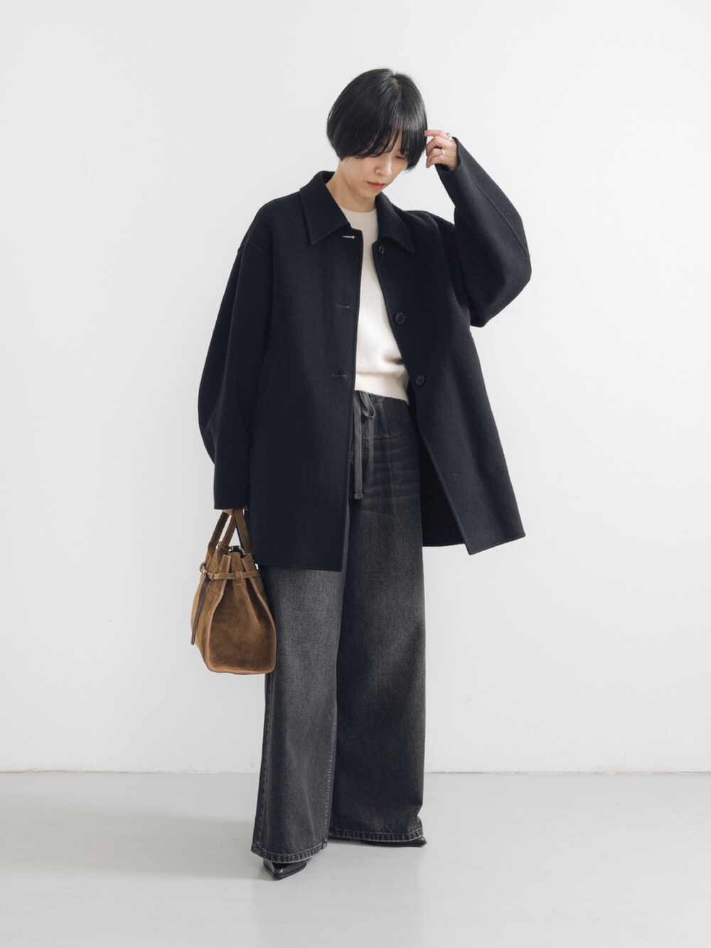 ホワイト系のベスト、ブラック系のステンカラーコート、ブラック系のデニムパンツを着用したレディースの秋コーディネートの2枚目の写真
