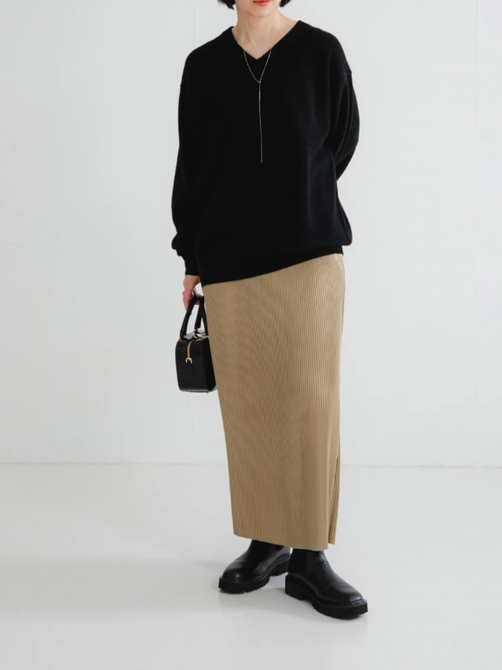 ブラック系のニット/セーター、ベージュ系のスカート、ブラック系のブーツを着用したレディースの冬コーディネートの2枚目の写真