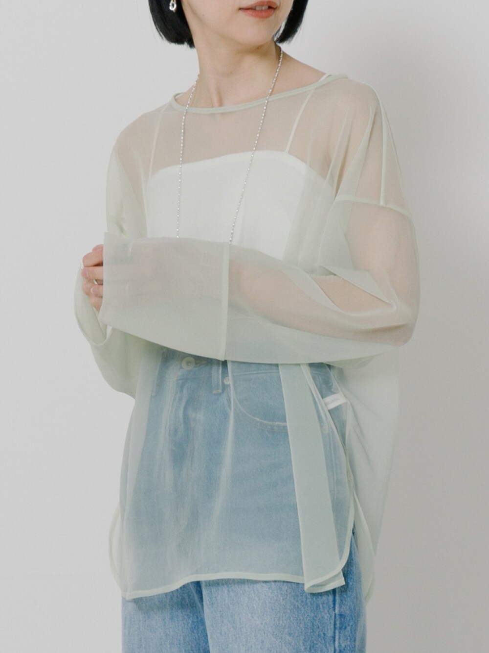 グリーン系のTシャツ/カットソー、ホワイト系のキャミソール、ブルー系のデニムパンツを着用したレディースの冬コーディネートの2枚目の写真