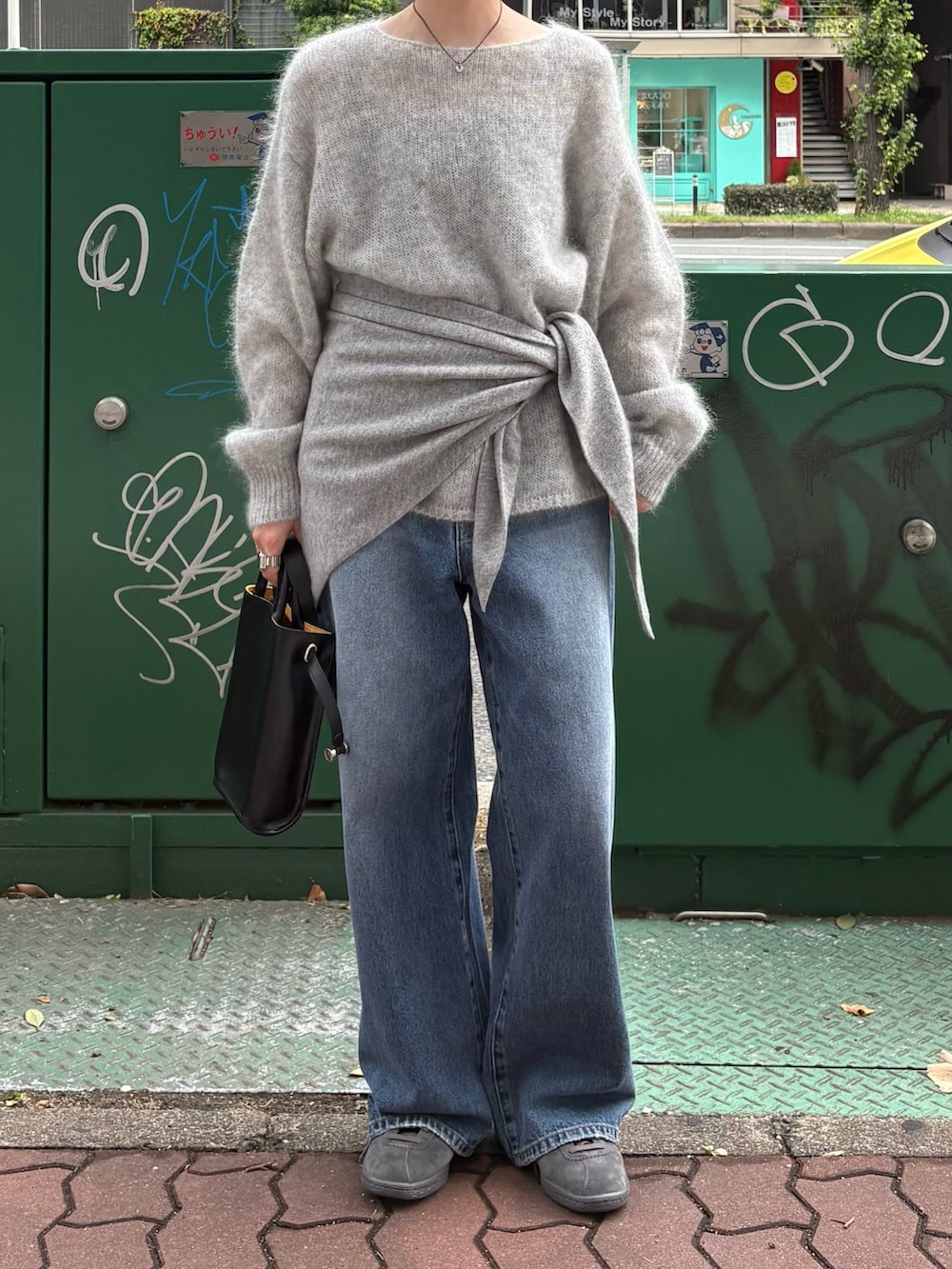 グレー系のニット/セーター、ブルー系のデニムパンツ、ブラック系のショルダーバッグを着用したレディースの秋コーディネートの2枚目の写真
