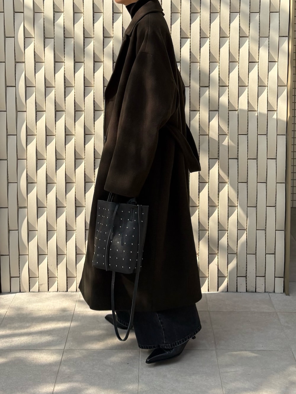 グリーン系のチェスターコート、ブラック系のニット/セーター、ブラック系のデニムパンツを着用したレディースの冬コーディネートの2枚目の写真