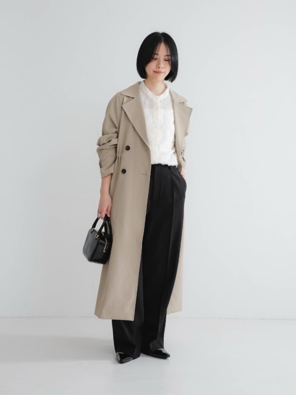 ブラック系のその他パンツ、ベージュ系のトレンチコート、ホワイト系のシャツ/ブラウスを着用したレディースの冬コーディネートの2枚目の写真