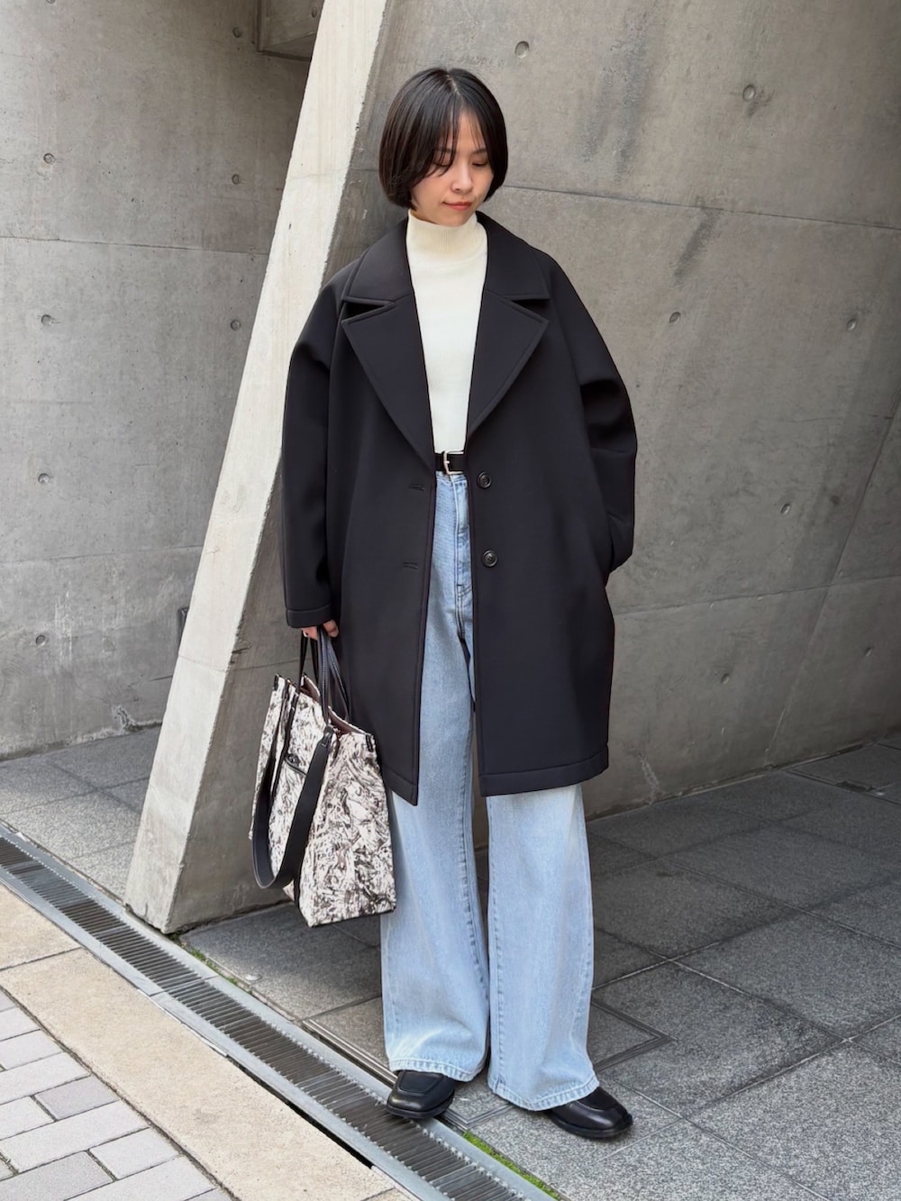 ブラック系のチェスターコート、ホワイト系のニット/セーター、ブラック系のローファーを着用したレディースの冬コーディネートの2枚目の写真